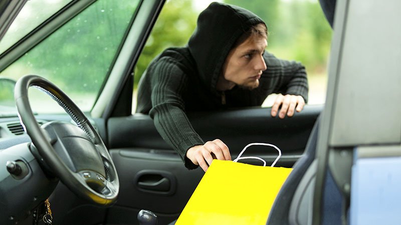 Tyv som strekker seg gjennom bilvinduet og stjeler verdisaker. 