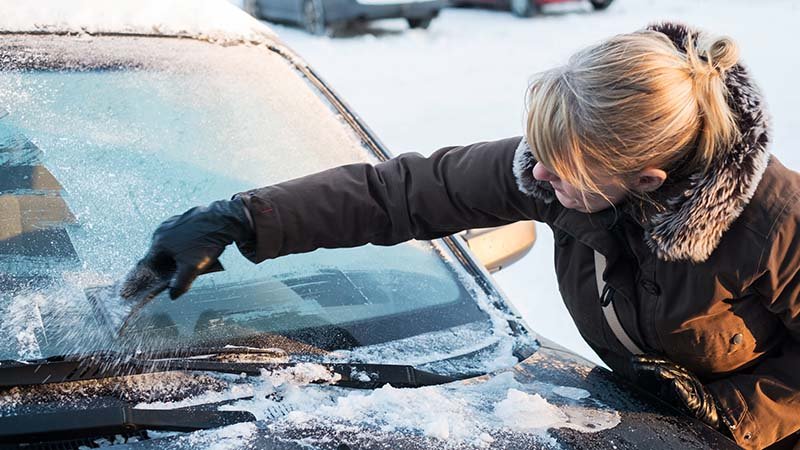 Dame skraper nediset frontrute på bil