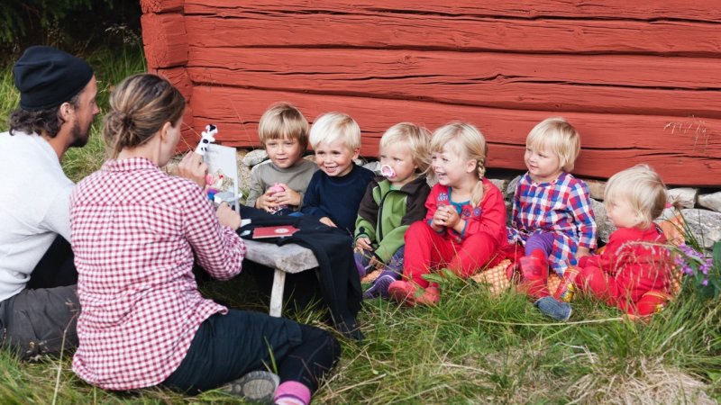 Barnehagebarn langs rødmalt husvegg.