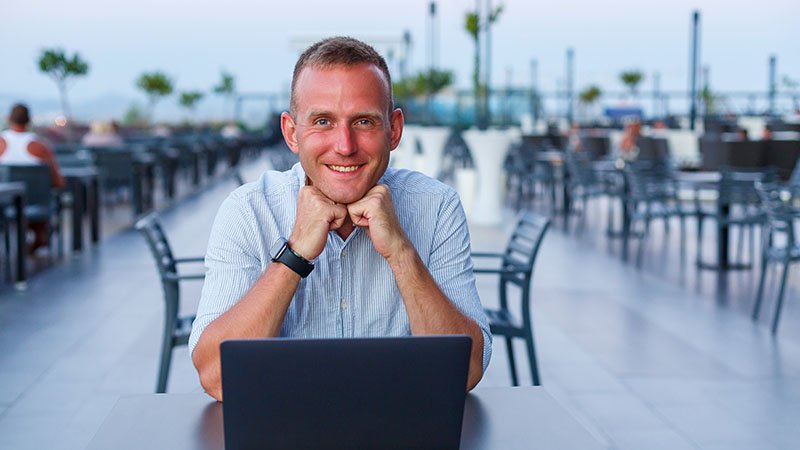 Mann ved pc på tom restaurant ved stranden.