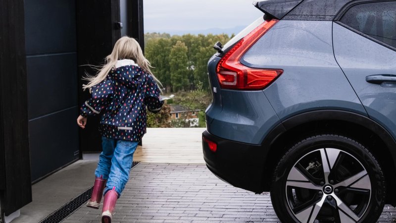 Barn løper rundt bil parkert utenfor garasje.