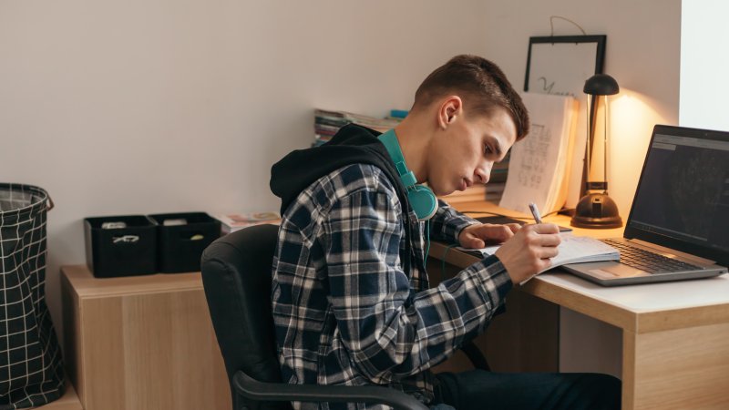 Bildet viser en ung gutt som sitter hjemme og jobber med skole