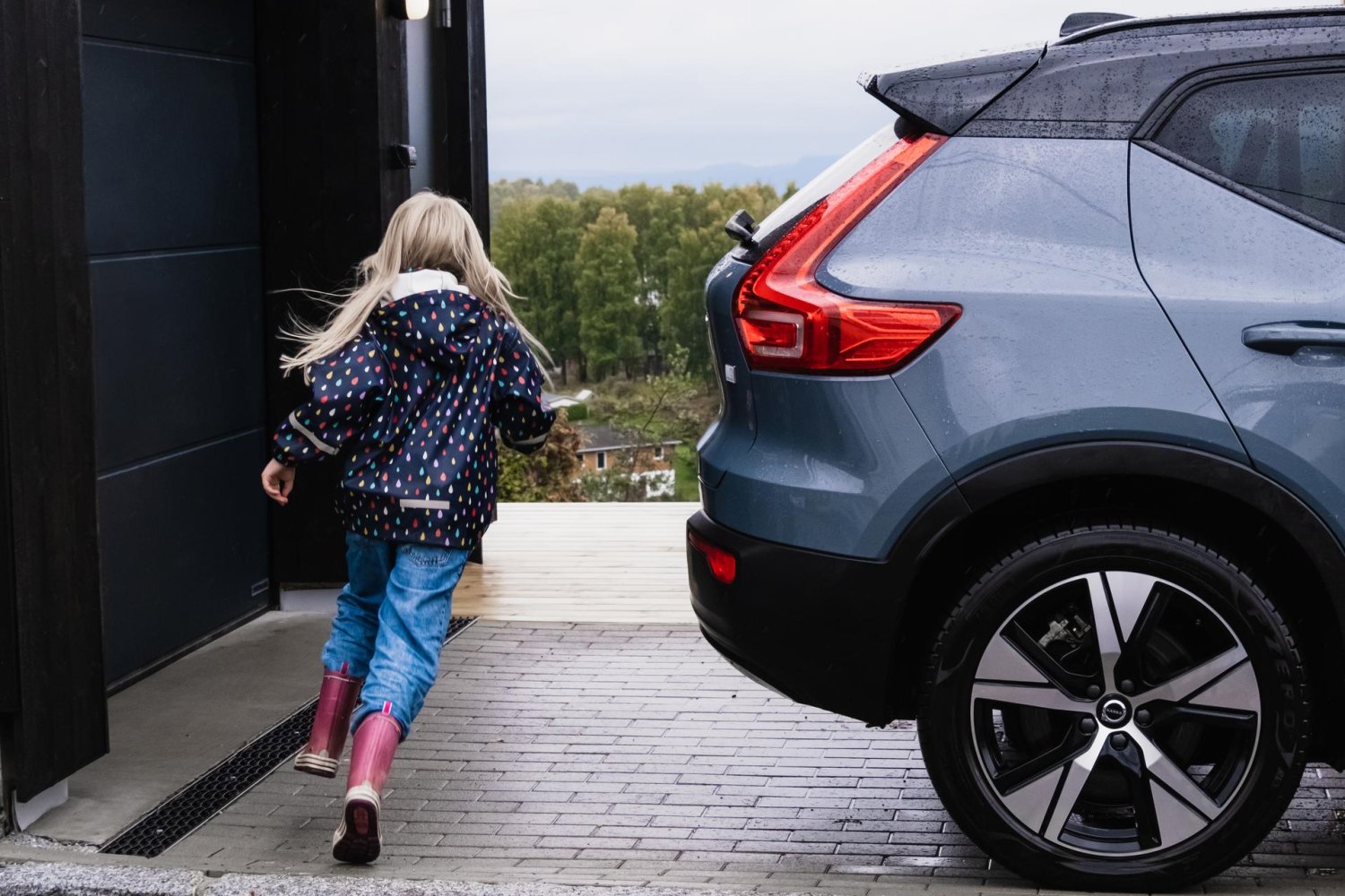 Barn løper rundt bil parkert utenfor garasje.