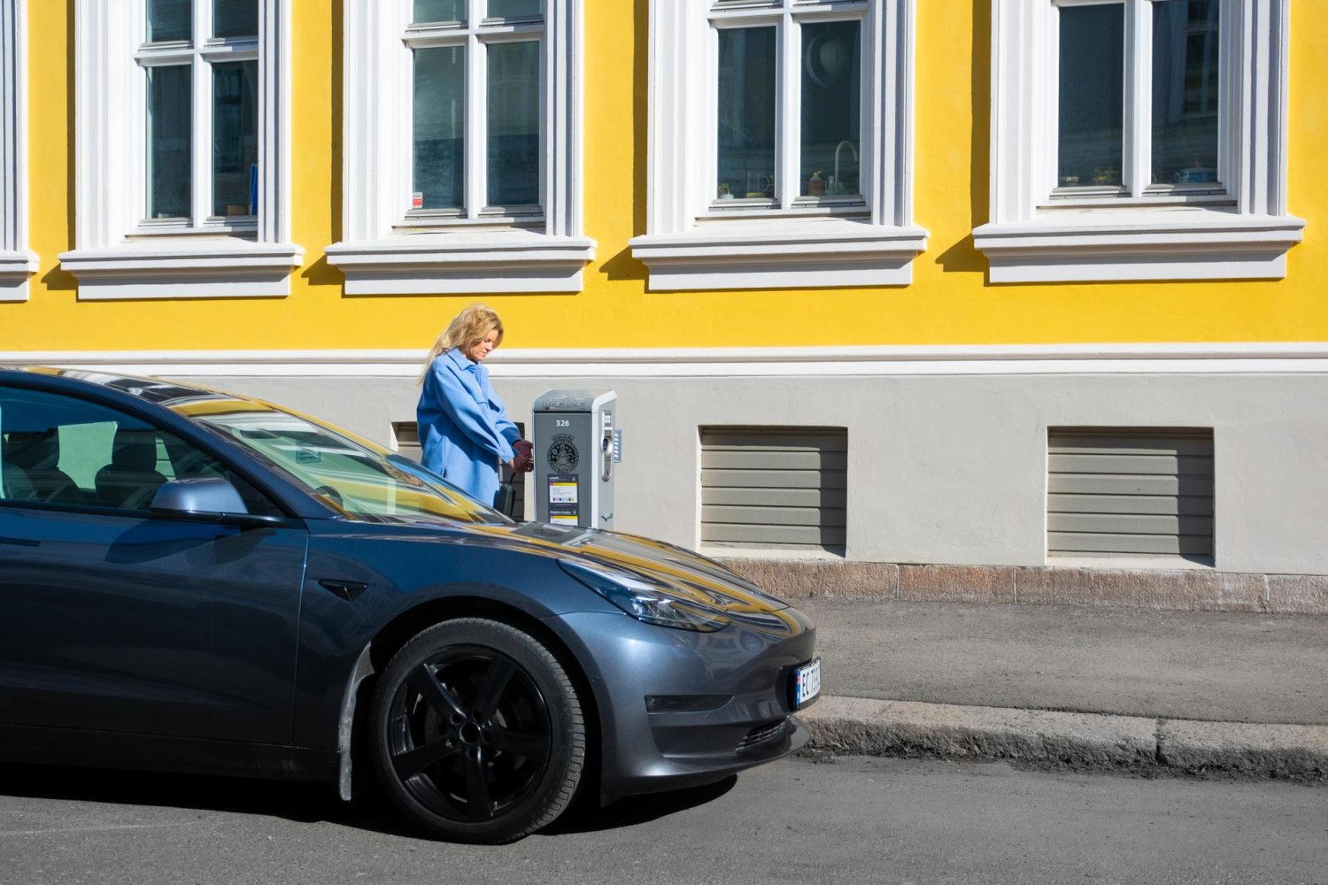 Kvinne kobler elbil til et ladepunkt i gata