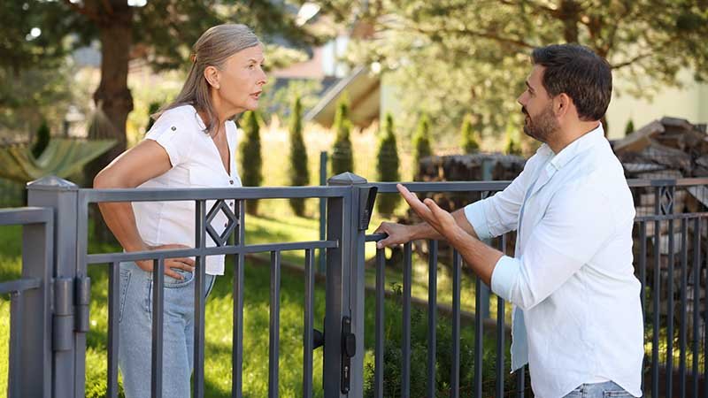 Naboer som diskuterer ivrig over hagegjerdet.