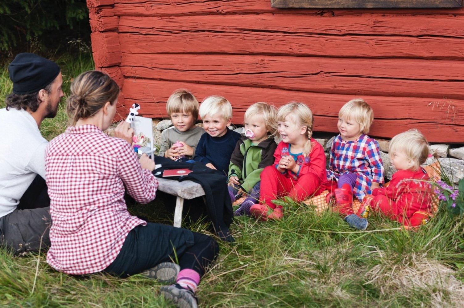 Barnehagebarn langs rødmalt husvegg.