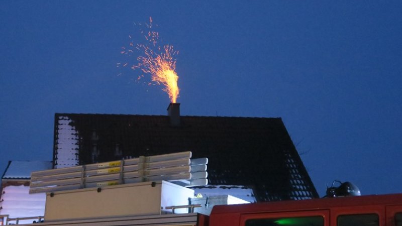 Gnister fyker ut av en skorstein på et hustak, med en brannbil i forgrunnen.