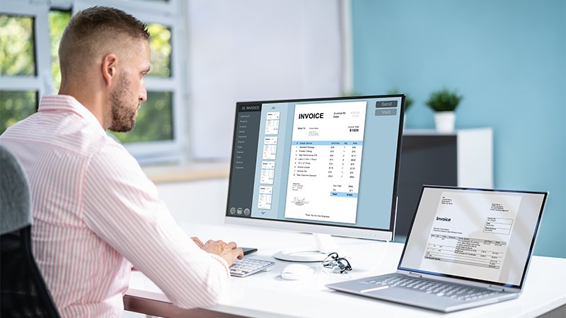 Mann på kontor med flere skjermer med fakturaer.